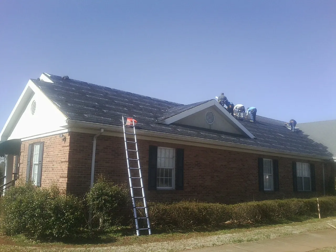 Crew tearing shingles off a brick ranch roof with a ladder set — Emergency Roof Repair work by our crew in Temple City