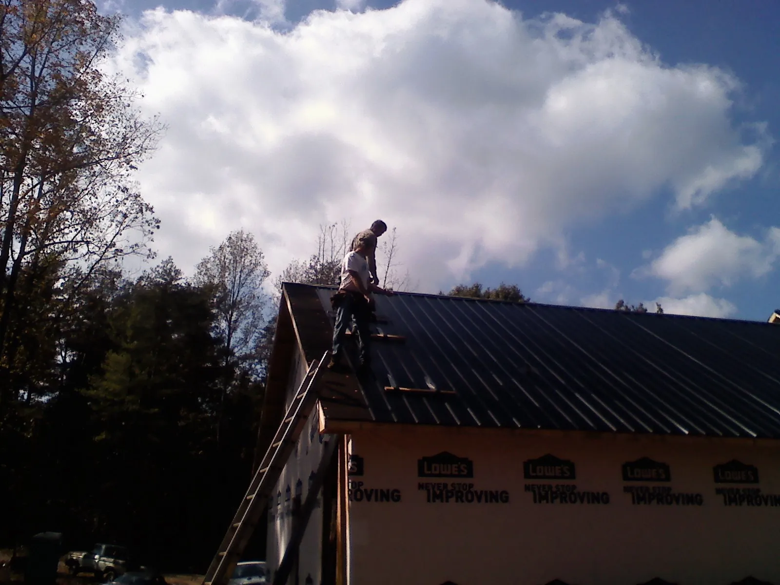 Roofer fastening dark metal panels high against a cloudy sky, from a Roof Inspection job in Temple City