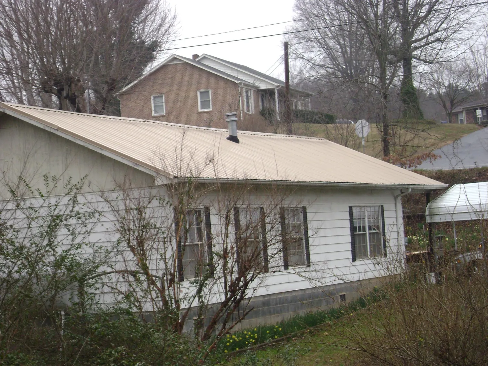Tan metal roof on a white sided house set into a hillside — Commercial Roofing by Roofing Brothers in Temple City
